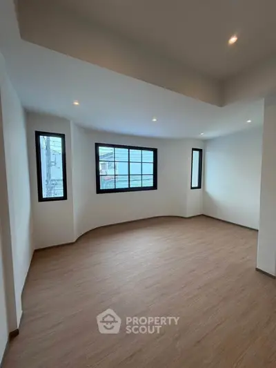 Spacious unfurnished room with large windows and wooden flooring, ideal for customization.