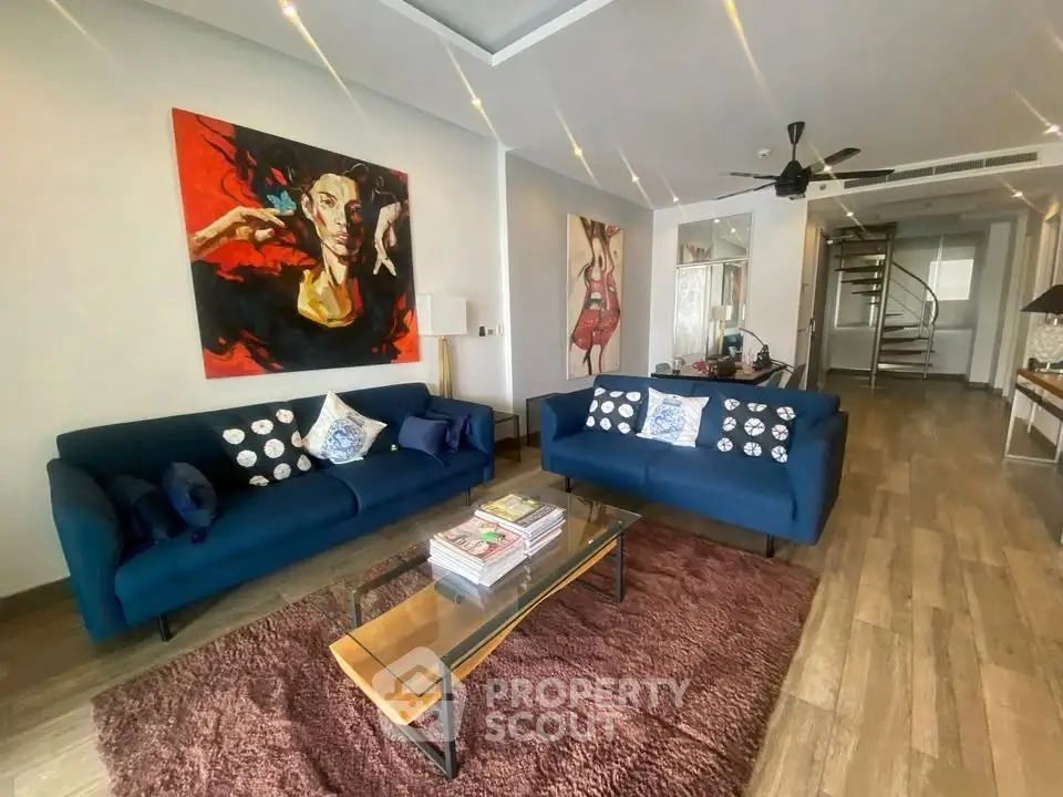 Stylish living room with modern art, blue sofas, and wooden flooring in a contemporary home.