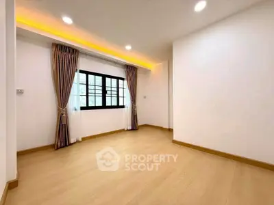 Spacious empty room with wooden flooring and large window, perfect for customization.