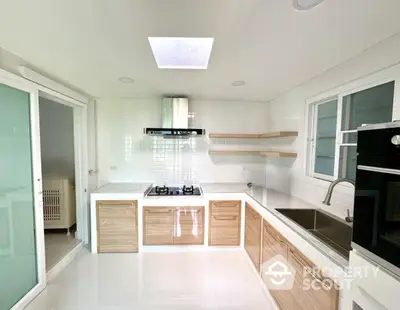 Modern kitchen with sleek cabinetry, gas stove, and built-in oven, featuring a skylight for natural illumination.