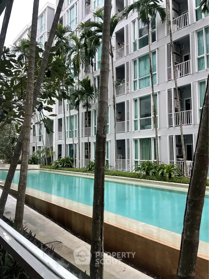 Modern apartment building with pool and lush palm trees, offering a serene urban oasis.