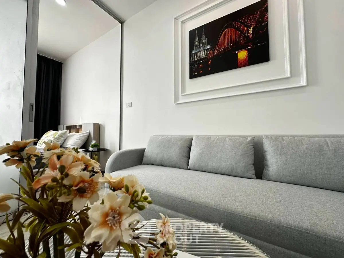 Modern living room with stylish decor and cozy gray sofa, featuring elegant wall art and fresh floral arrangement.