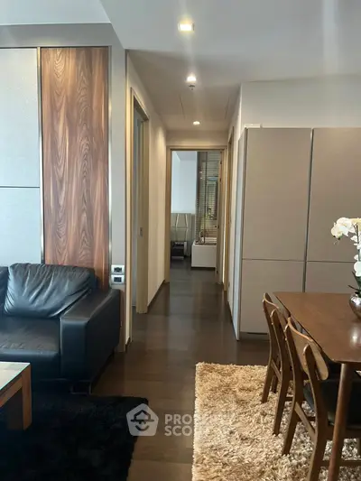 Modern apartment interior with sleek living room and dining area, featuring dark wood flooring and elegant furniture.