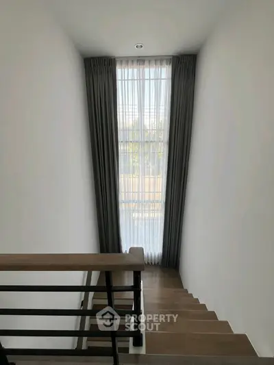 Elegant staircase with tall window and modern railing in a bright home interior.