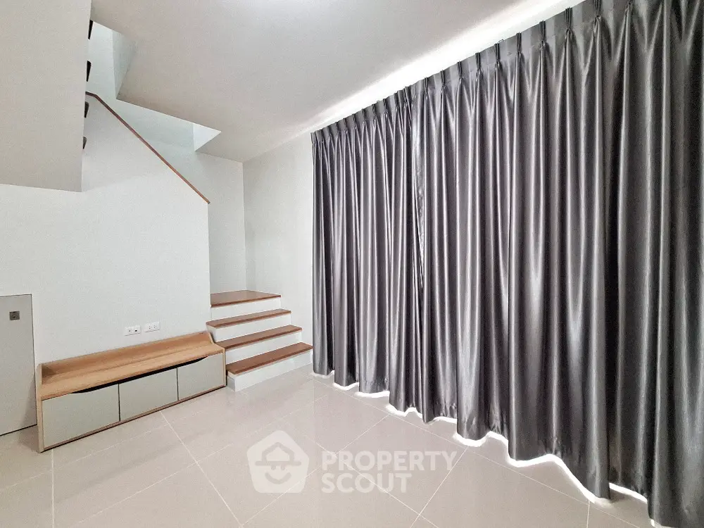 Spacious and modern living room with elegant dark curtains and clean white tiled flooring, featuring a unique staircase leading to an upper level.