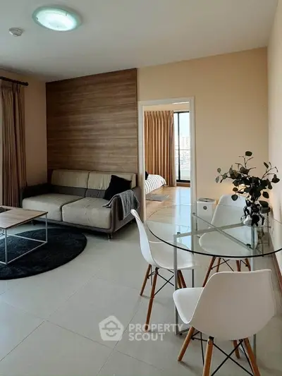 Modern living room with stylish furniture and open view to bedroom, featuring a cozy sofa and glass dining table.