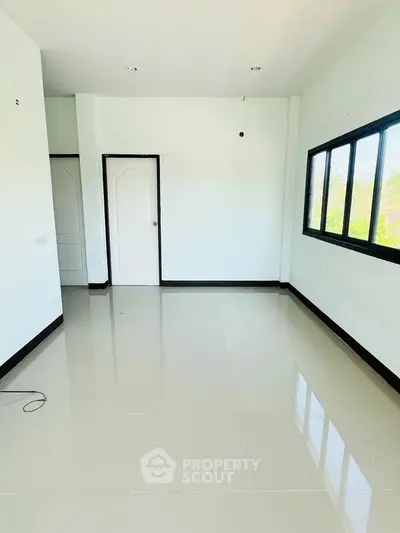 Spacious empty room with glossy tiled floor and large windows offering natural light.