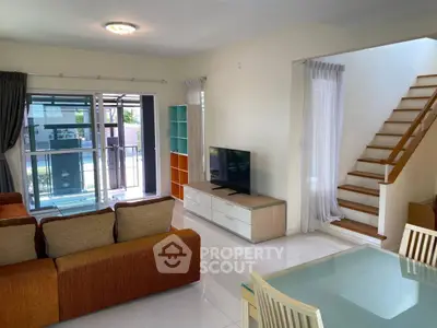 Spacious living room with modern furniture and natural light, featuring a staircase and balcony access.