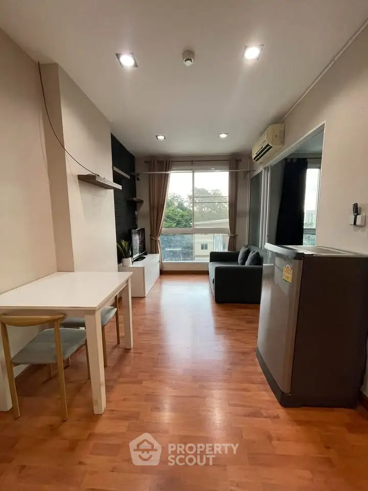 Modern living room with wooden flooring and large window, featuring a cozy sofa and dining area.