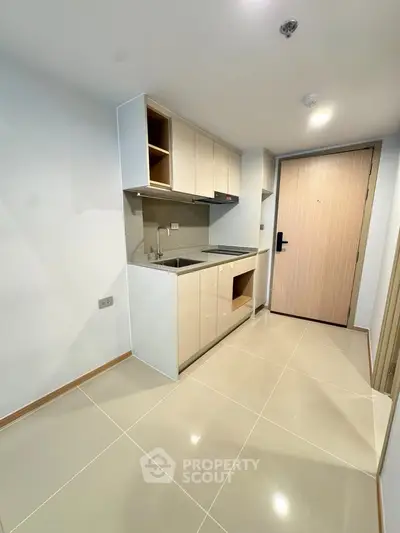 Modern compact kitchen with sleek cabinetry and tiled flooring in a contemporary apartment.