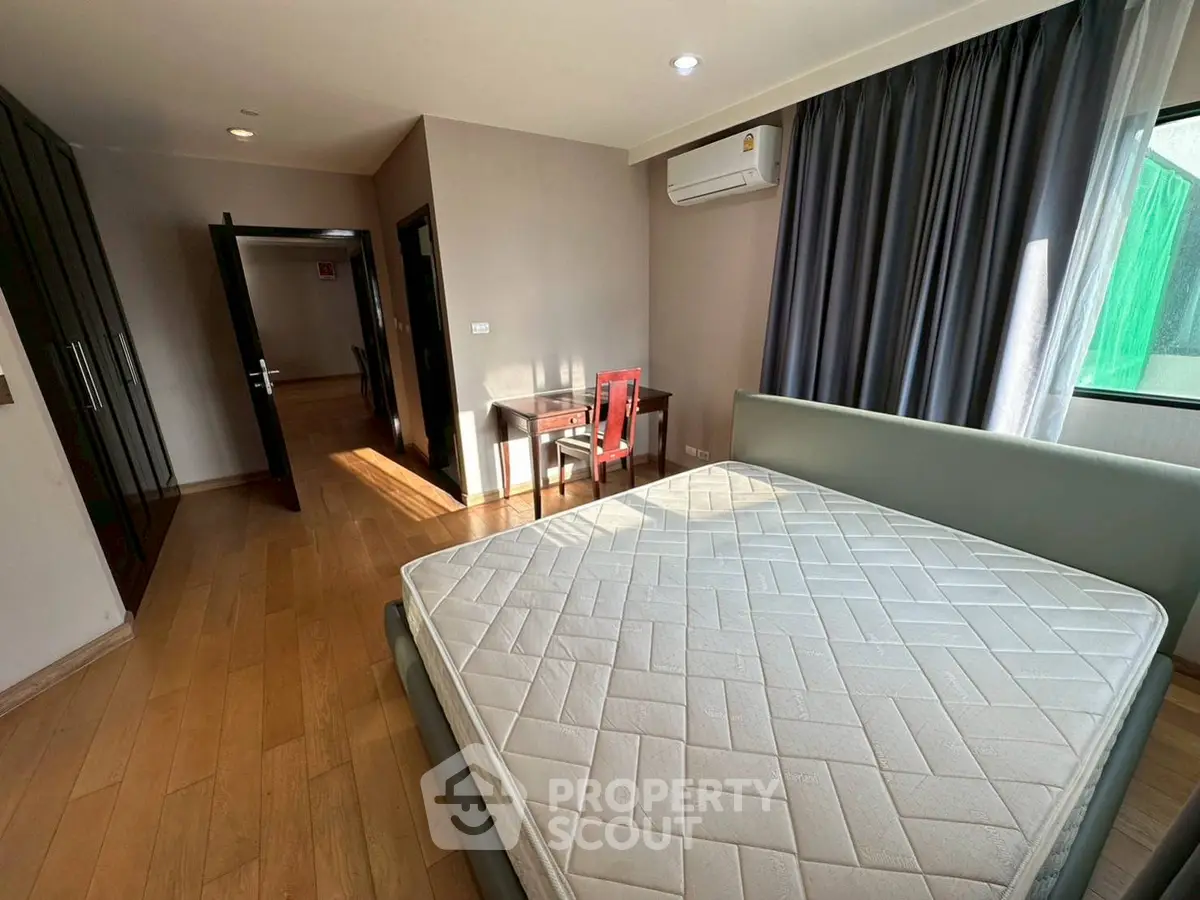 Spacious bedroom with wooden flooring and natural light in modern apartment