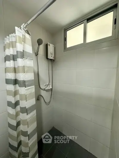 Modern bathroom with shower and striped curtain, featuring a compact water heater and frosted window.