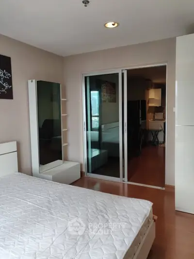 Modern bedroom with sliding glass doors leading to a stylish kitchen area, featuring sleek furnishings and wooden flooring.