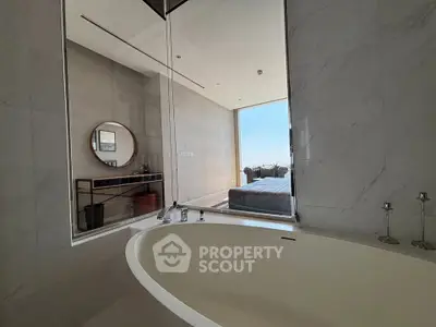 Luxurious bathroom with a sleek bathtub and a view into a modern bedroom with natural light.