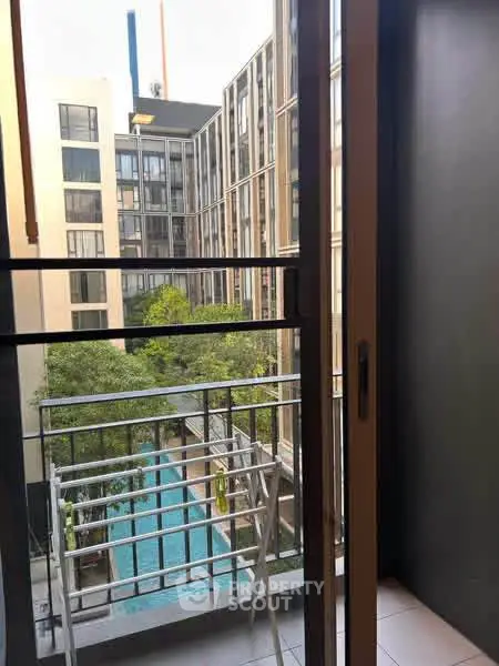 Modern apartment view with balcony overlooking pool and lush greenery.