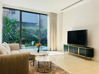 Luxurious living room with modern decor and garden view, featuring elegant furniture and large windows.
