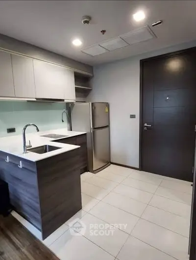 Modern kitchen with sleek cabinetry and stainless steel fridge in compact apartment.
