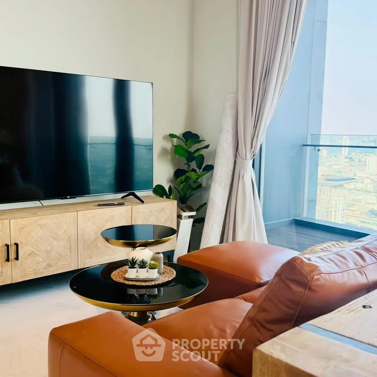 Modern living room with leather sofa, large TV, and stunning city view from balcony.