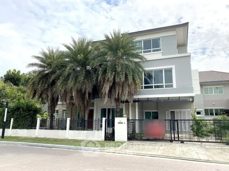 Modern two-story house with palm trees and gated entrance in a suburban neighborhood.