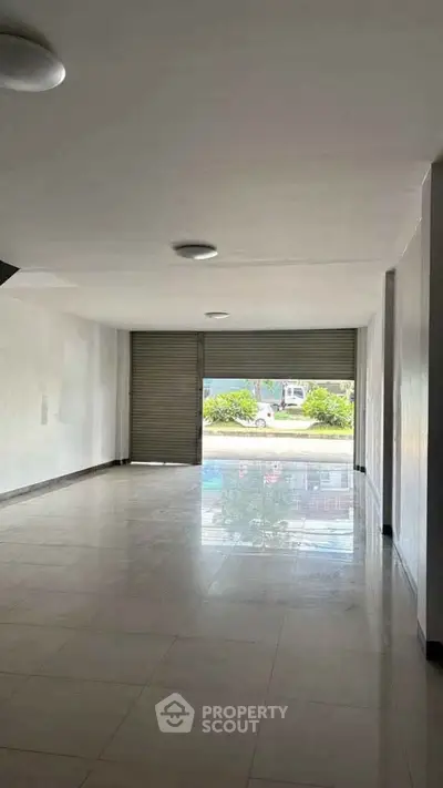 Spacious empty room with large window and tiled floor, ideal for commercial use.