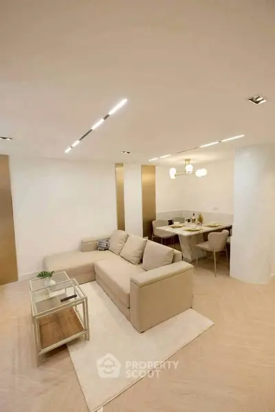 Modern living room with beige sofa and elegant dining area, featuring contemporary lighting and sleek design.