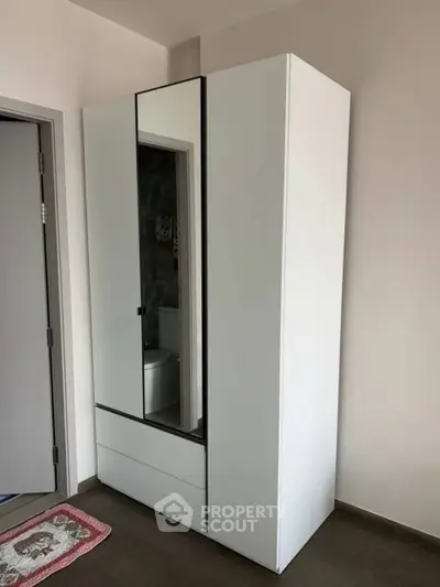 Modern white wardrobe with mirror in a minimalist bedroom setting.