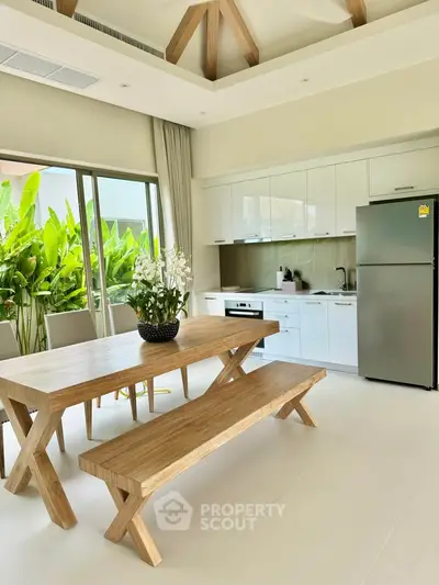 Modern kitchen with open layout and stylish dining area, featuring natural light and lush greenery view.