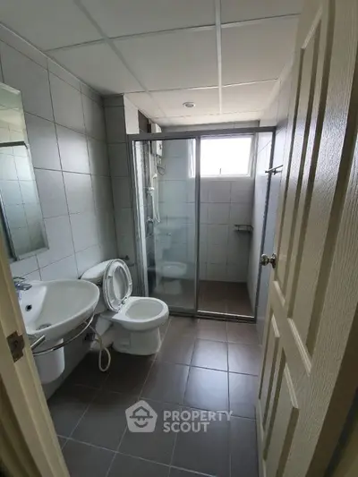 Modern bathroom with glass shower and tiled walls, featuring sleek fixtures and natural light.