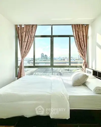 Bright bedroom with large windows offering stunning city views, featuring elegant curtains and cozy bedding.