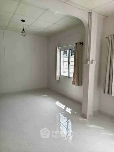 Bright and airy room with large window and modern light fixture, perfect for versatile living space.
