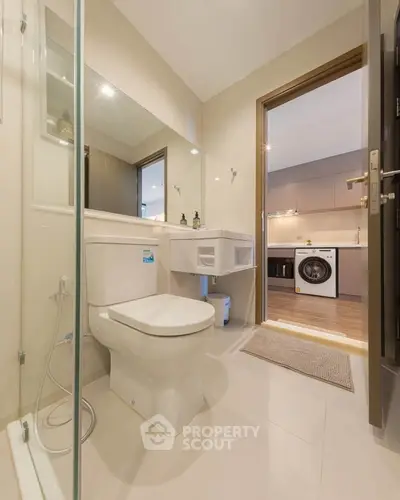 Modern bathroom with view into sleek kitchen featuring washing machine.