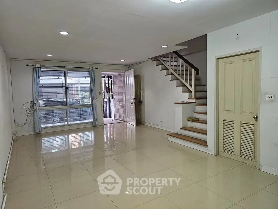 Spacious living room with glossy tiled floors and staircase in modern home.