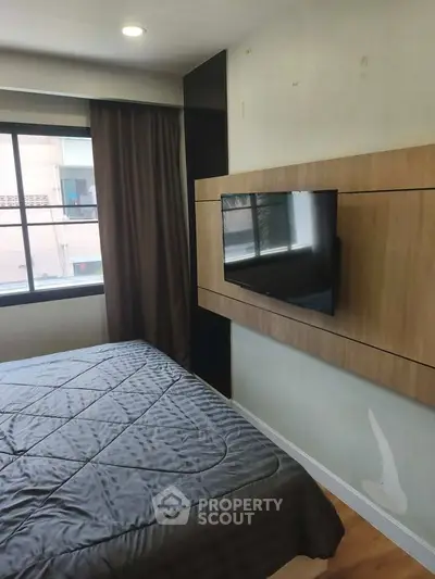 Modern bedroom with wall-mounted TV and large window for natural light.