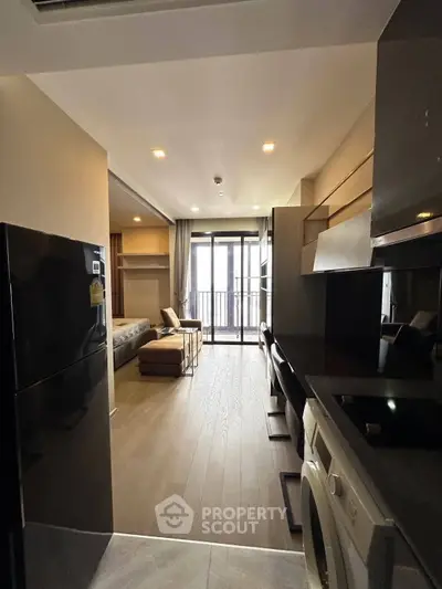 Modern studio apartment with open layout, featuring a sleek kitchen and cozy living area leading to a balcony.