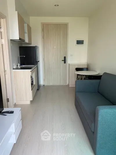 Modern compact living room with kitchenette in a cozy apartment, featuring sleek furniture and minimalist design.