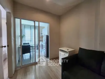 Cozy living room with sliding glass doors leading to a modern kitchen, featuring a sleek black sofa and wooden flooring.