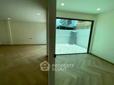 Spacious modern living room with glass doors leading to a private balcony, featuring elegant wood flooring.