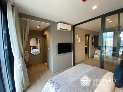 Spacious bedroom with modern design, featuring a large bed, sleek flat-screen TV, and access to a sunny balcony with a view, creating a perfect urban retreat.