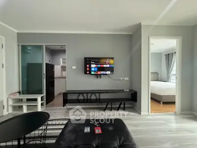 Modern living room with sleek TV setup and view into a cozy bedroom, showcasing open layout and stylish decor.