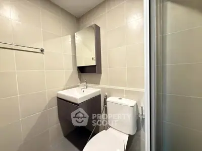 Modern bathroom with sleek fixtures and neutral tiles, featuring a compact vanity and toilet.