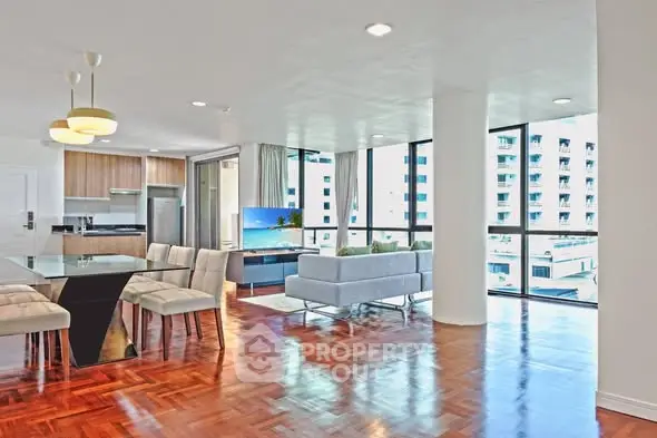 Spacious modern living room with open kitchen and large windows offering city views.