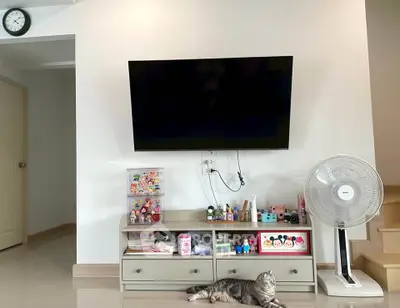 Modern living room with wall-mounted TV, fan, and decorative items on a cabinet.