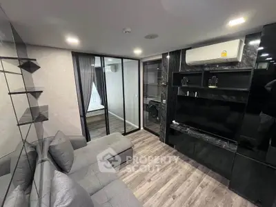 Modern living room with sleek black cabinetry and cozy gray sofa, featuring a view into a stylish bedroom.