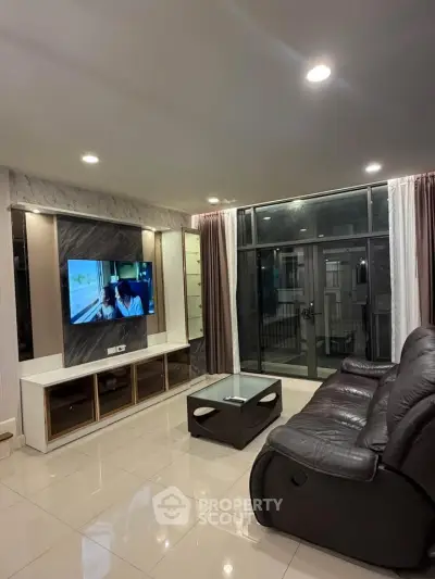 Modern living room with sleek furniture and large TV, featuring elegant lighting and floor-to-ceiling windows.