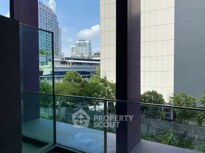 Modern urban view from a glass balcony overlooking city buildings and greenery.