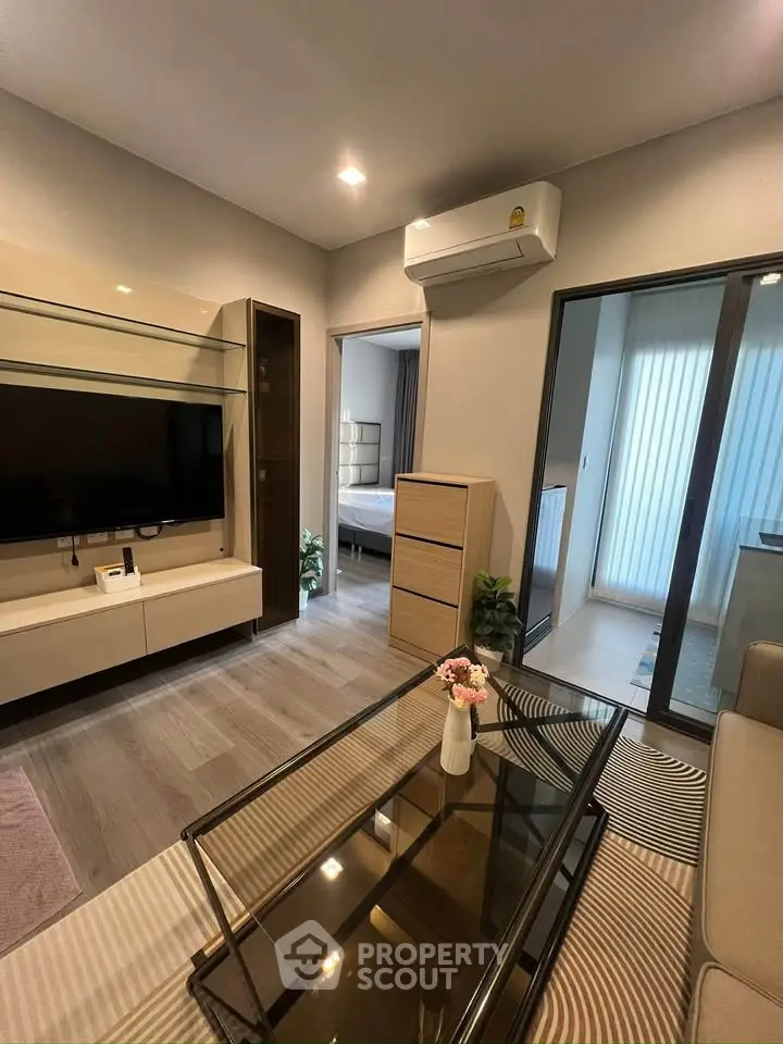 Modern living room with sleek furniture and glass coffee table, leading to a cozy bedroom.
