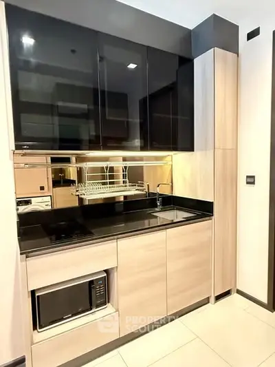 Modern compact kitchen with sleek black and wood cabinetry, featuring built-in microwave and stylish backsplash.