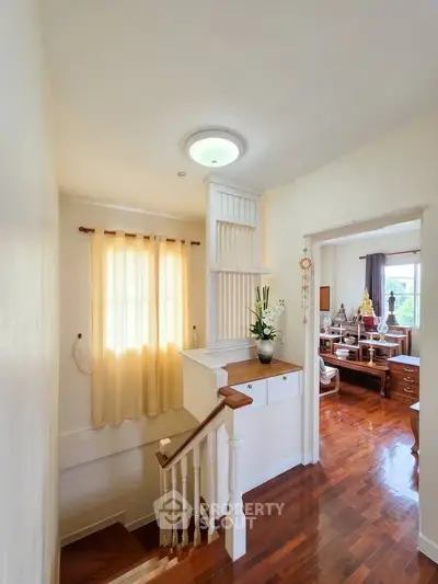 Bright hallway with wooden floors leading to a cozy living area with natural light.