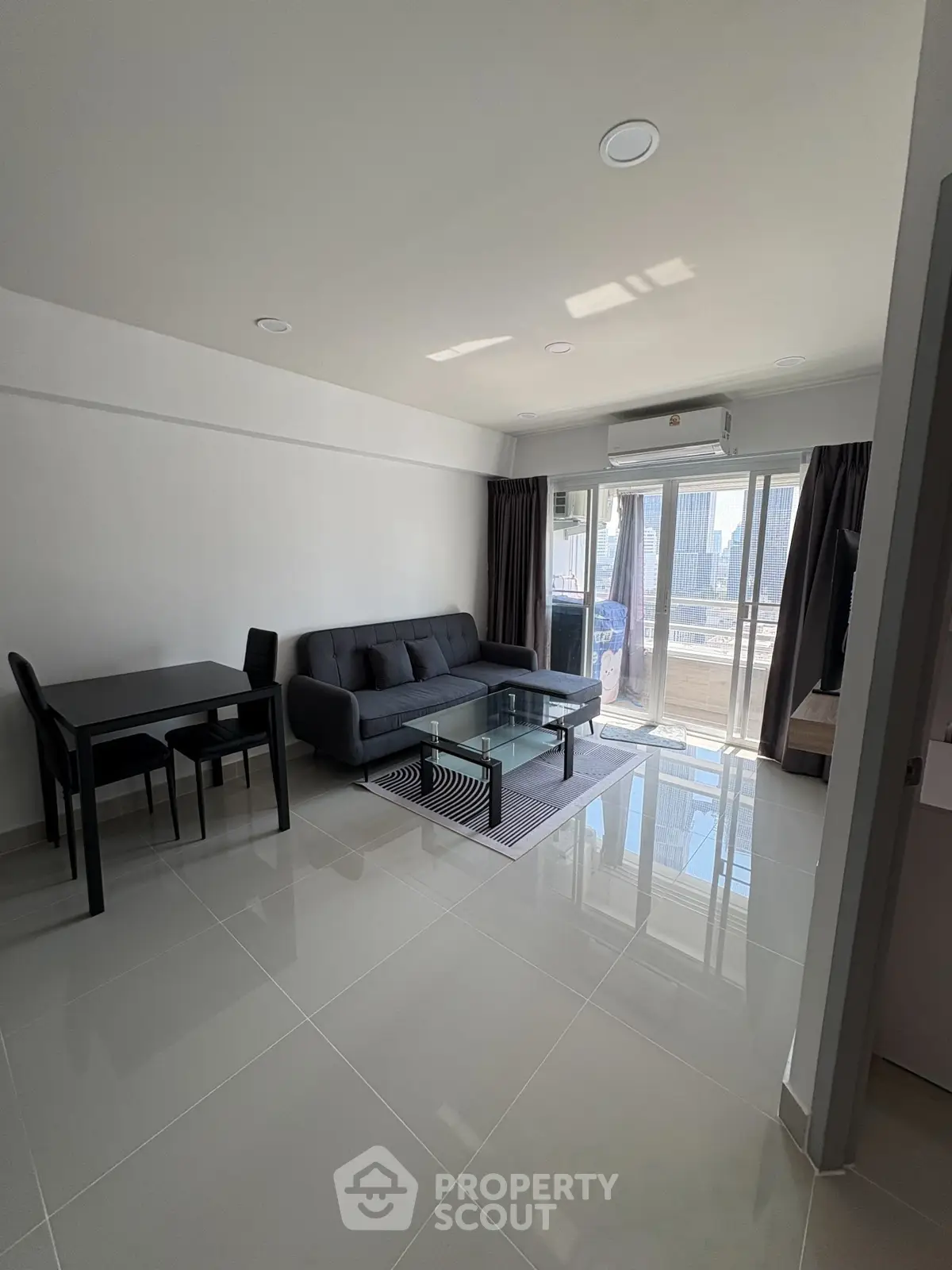Modern living room with sleek furniture and city view balcony in high-rise apartment.
