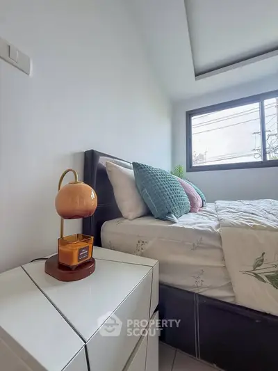 Cozy bedroom with modern decor and natural light, featuring a stylish bedside lamp and plush pillows.